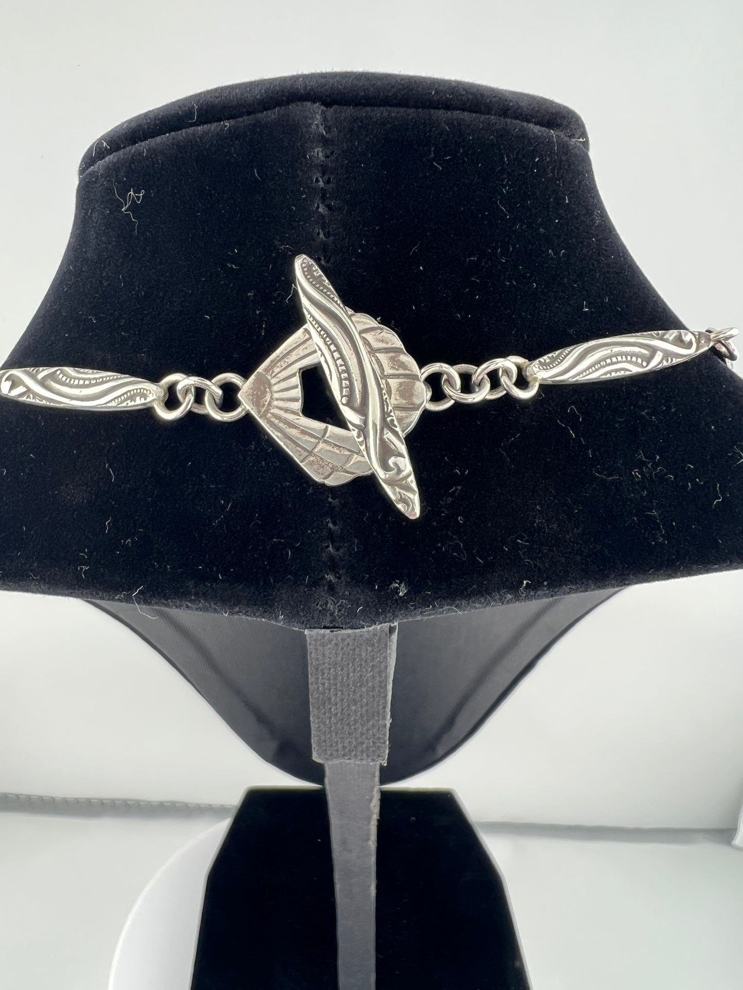 Silver necklace with a unique design on a black velvet stand.