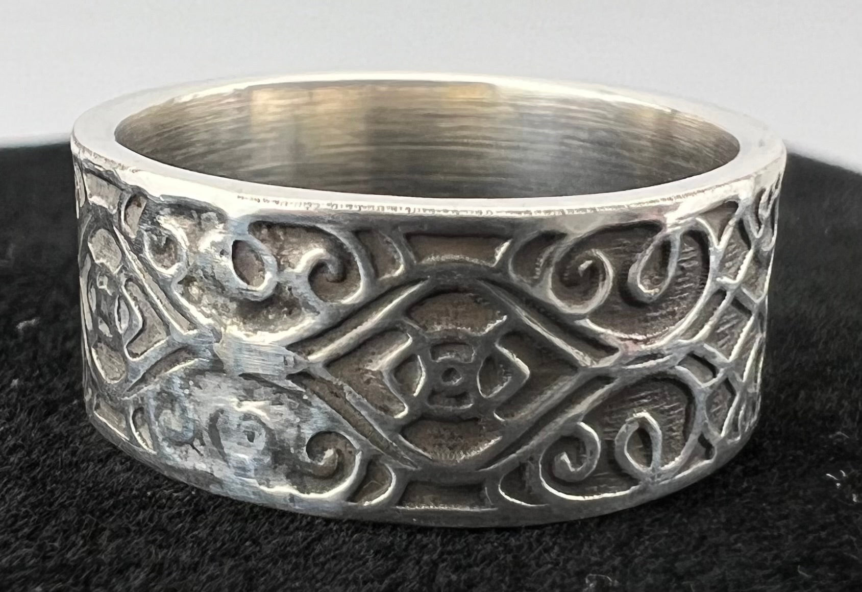 Silver ring with intricate patterns on a dark surface