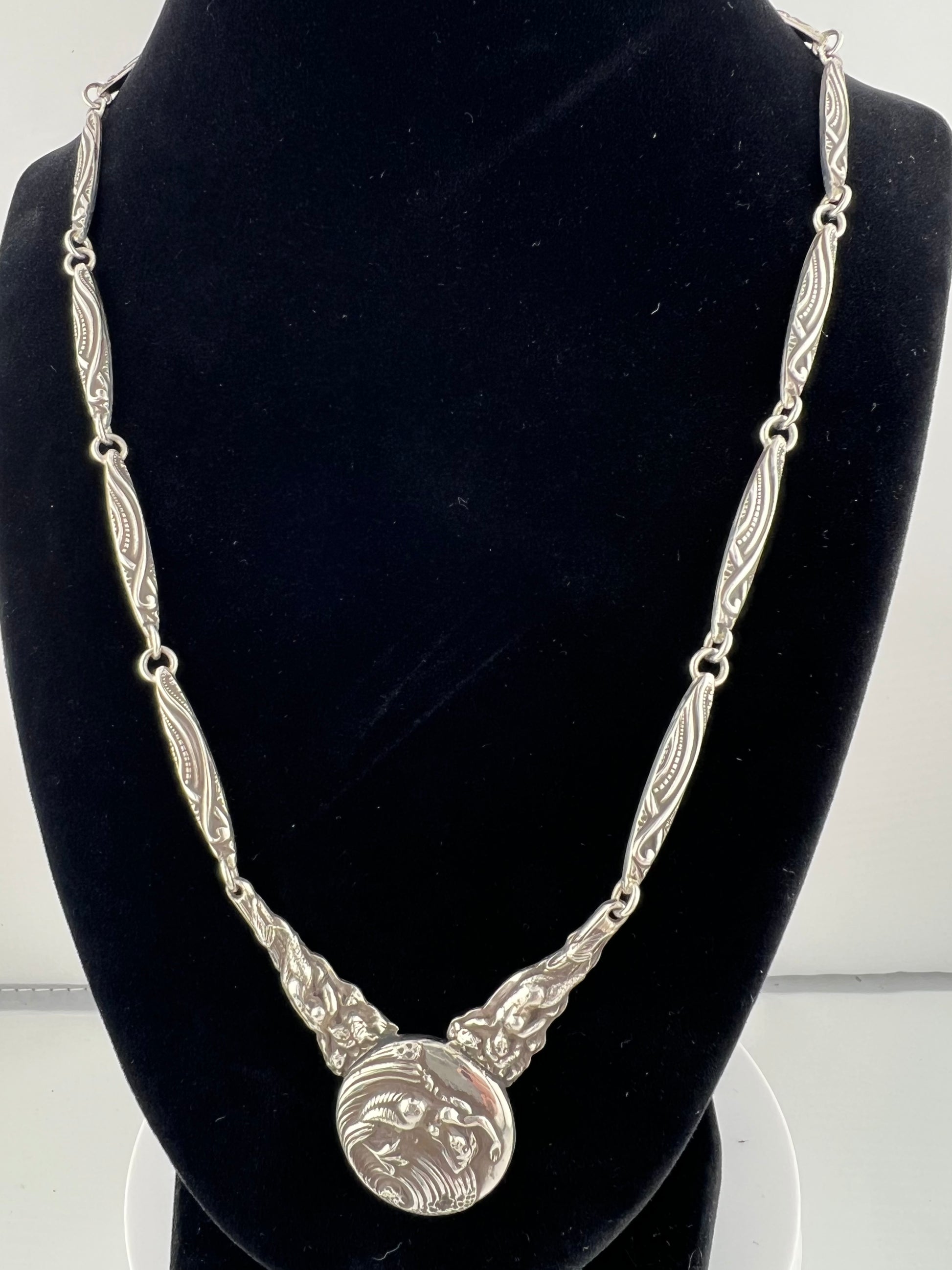 Silver necklace with mermaid on a black mannequin bust.