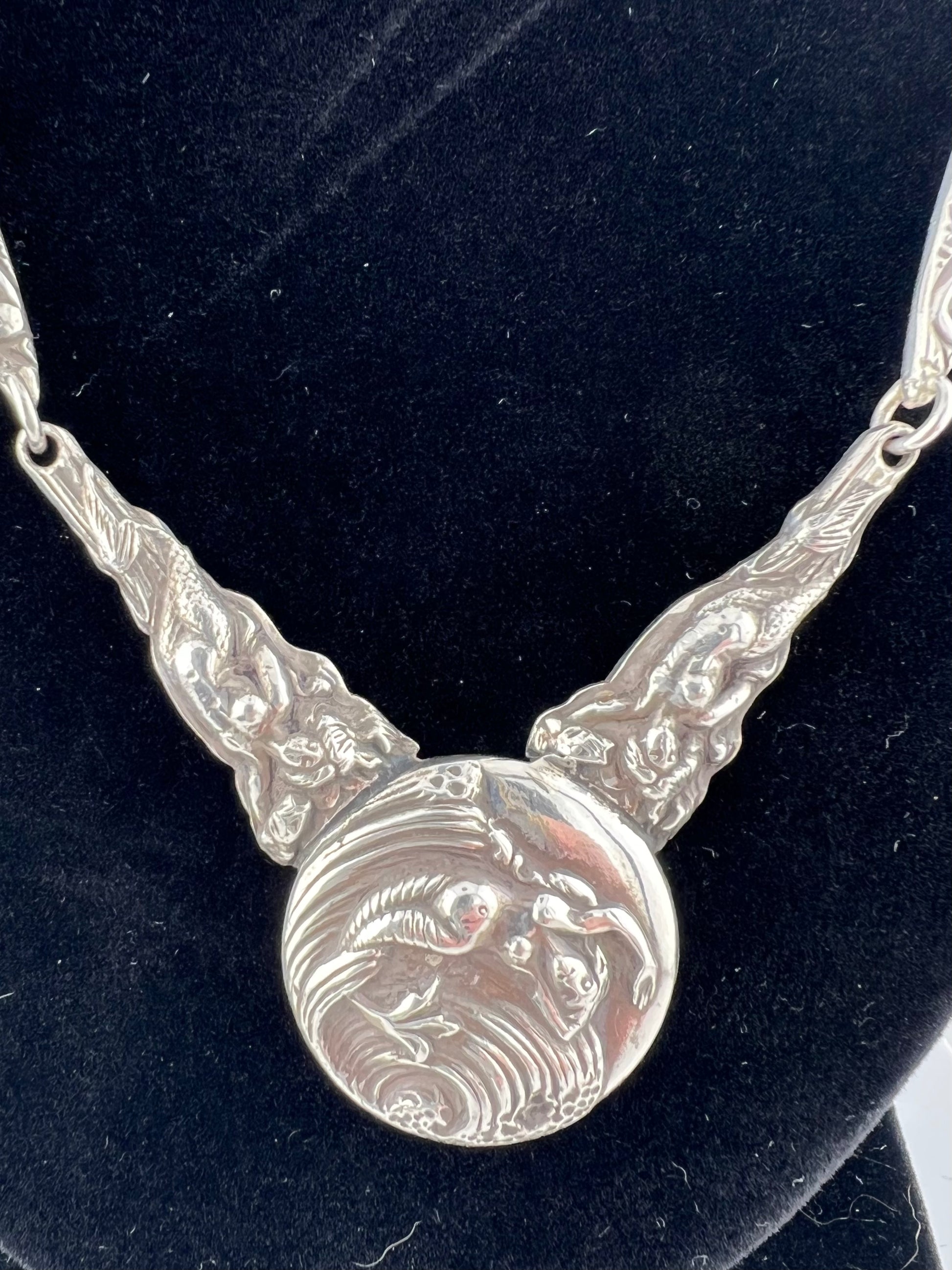 Silver necklace with mermaid design on a black background